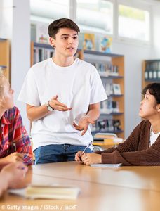 Junge spricht vor einer Gruppe Mitschüler.